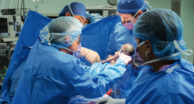 OB/GYN staff completing delivery of newborn by caesarean section.